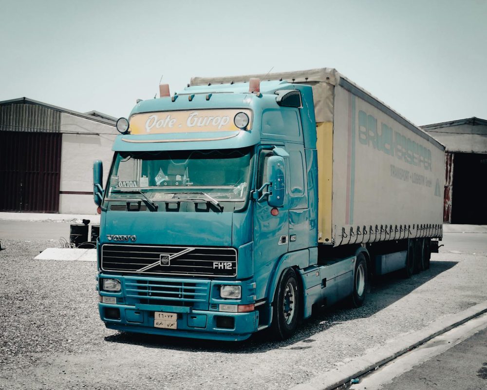 Transporte Santana Carrasco Valdeolmos - A blue Volvo truck parked outside a warehouse in an industrial area, daytime scene.